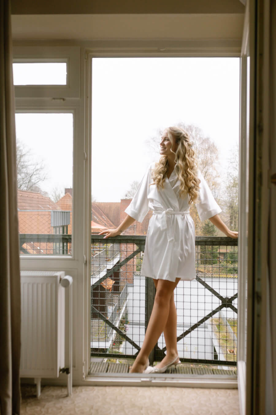 Die Braut steht beim Getting Ready mit der Hochzeitsfotografin Laura von Kaiserlich Fotografie auf dem Balkon