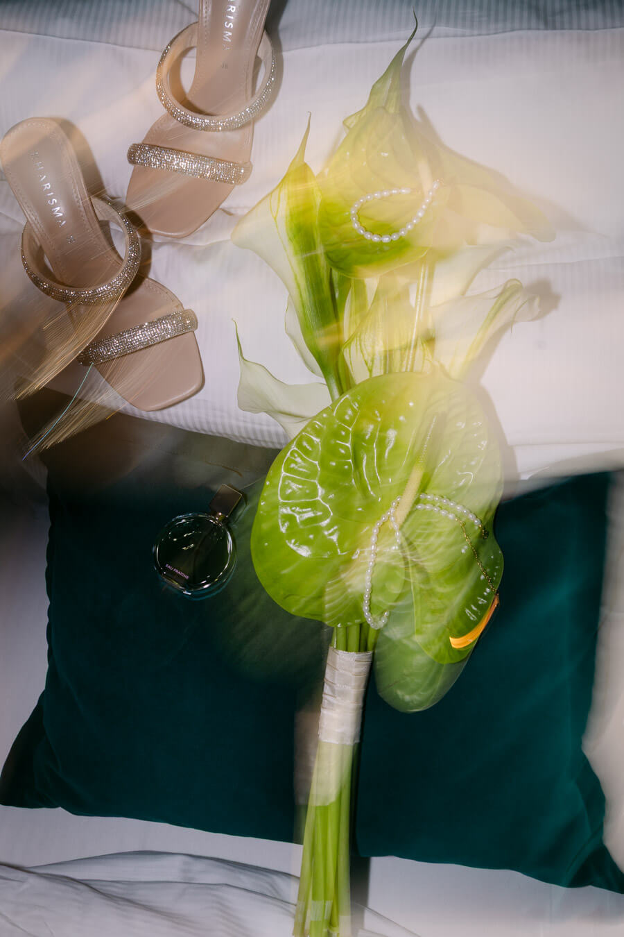 Die Brautschuhe und der Brautstrauß liegen auf dem Bett, das Bild wurde mit einem verwischten Effekt und Blitzlicht beim Getting Ready mit der Hochzeitsfotografin aus Hamburg Kaiserlich Fotografie aufgenommen
