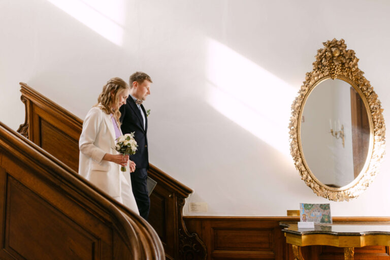 Das Brautpaar schreitet nach der standesamtlichen Hochzeit in Schloss Ahrensburg die Treppe herunter, das Licht fällt durch das Fenster hinein und berührt auch den antiken Spiegel