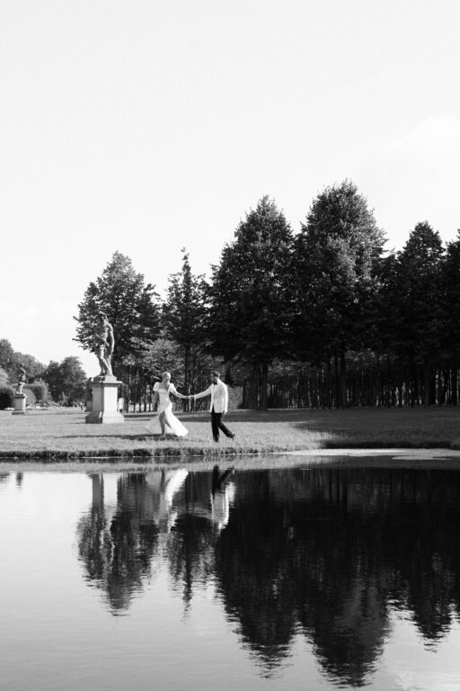 Das Brautpaar läuft am Wasser im Schlosspark, sie spiegeln sich im Wasser.