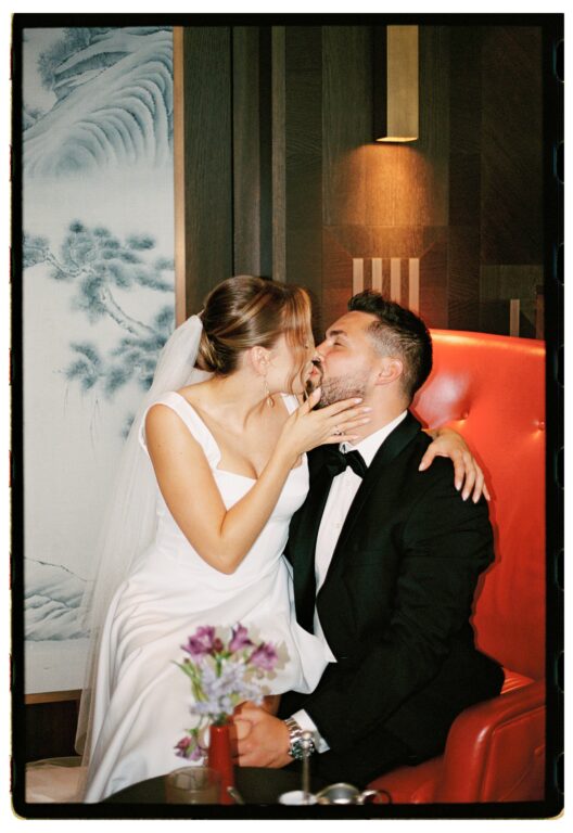 Das Brautpaar sitzt in der Hotellobby auf einem roten Sessel, die Braut küsst den Bräutigam, snslog fotografiert.