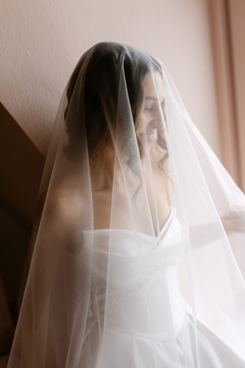 Die Braut trägt einen Schleier vor dem Gesicht und lächelt.