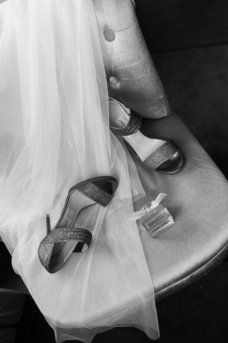 Die Brautschuhe liegen auf dem Stuhl zusammen mit dem Schleier und Parfüm wirkt es zufällig.