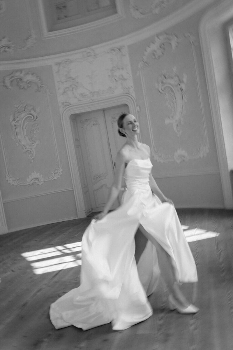 Die Braut läuft lachend durch den Saal des Prinzenhauses, das Bild ist schwarz weiß und leicht blurry.